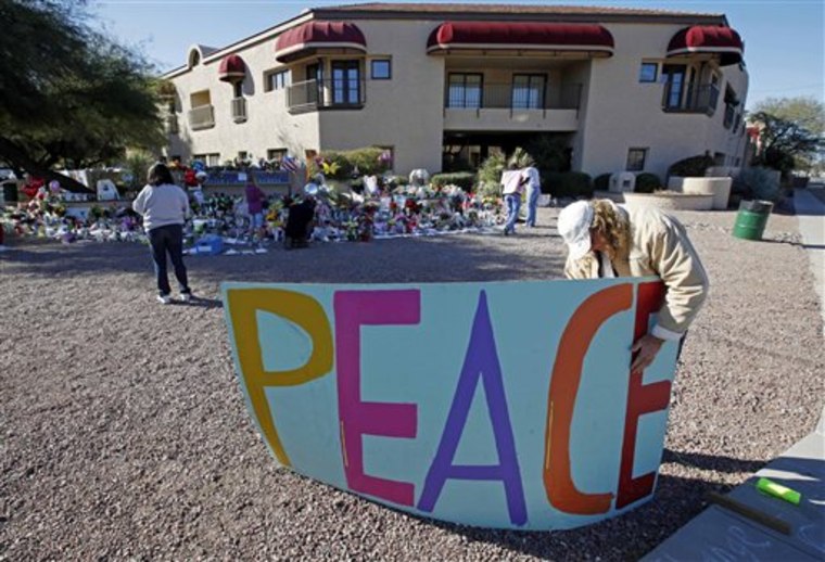 FILE - In this Jan. 12, 2011 file photo, Troy Wine puts up a peace sign at a makeshift memorial outside the office of Rep. Gabrielle Giffords, D-Ariz., , in Tucson, Ariz. The congresswoman's shooting has left some in Arizona questioning the identity and ideals of a state that has come to exemplify a radical, antiestablishment, we'll-do-things-our-way approach to governing. (AP Photo/Chris Carlson, File)
